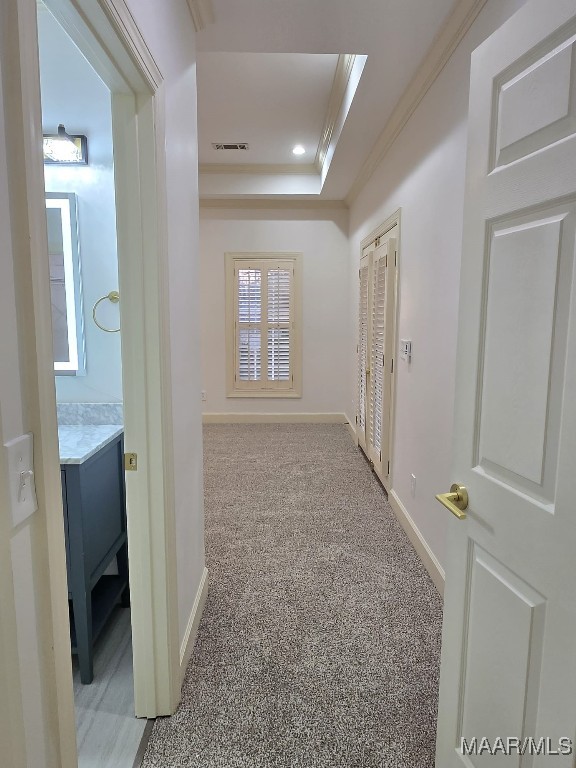 hallway with baseboards, visible vents, crown molding, light colored carpet, and a raised ceiling