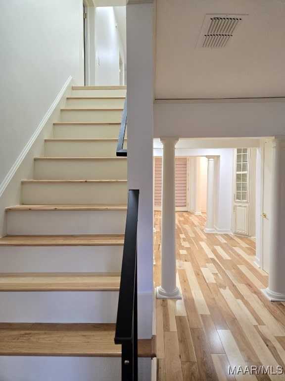 stairs featuring visible vents, wood finished floors, and ornate columns