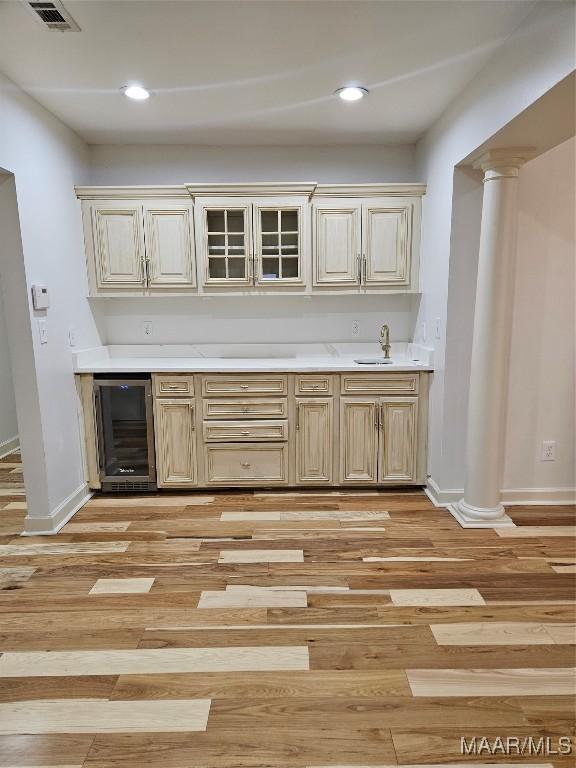 kitchen featuring visible vents, wine cooler, light countertops, decorative columns, and light wood-style floors