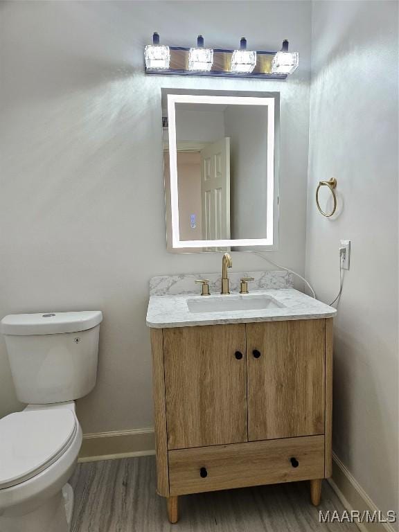 bathroom with toilet, vanity, baseboards, and wood finished floors