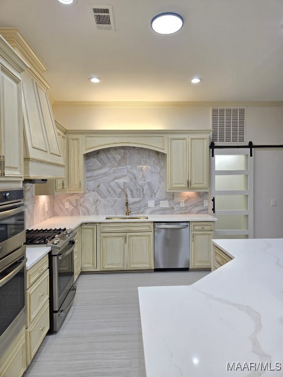 kitchen with visible vents, a sink, tasteful backsplash, cream cabinets, and stainless steel appliances