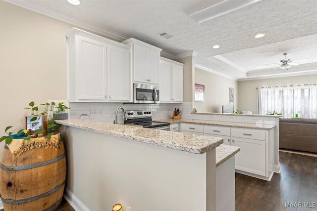 kitchen with a raised ceiling, a peninsula, white cabinetry, and appliances with stainless steel finishes