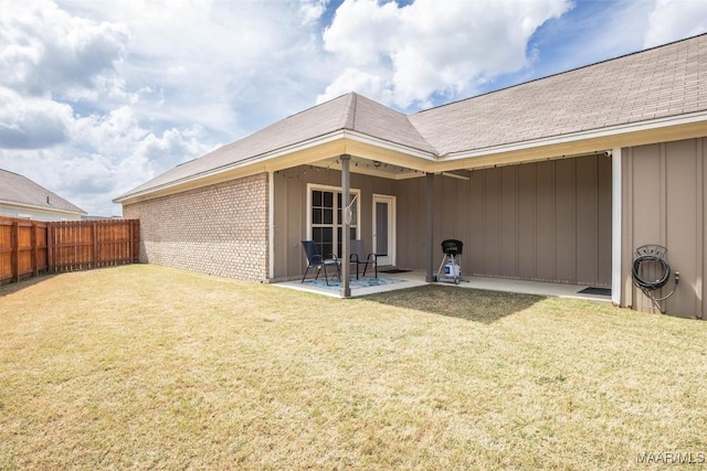 rear view of property featuring a patio, fence, a yard, board and batten siding, and brick siding