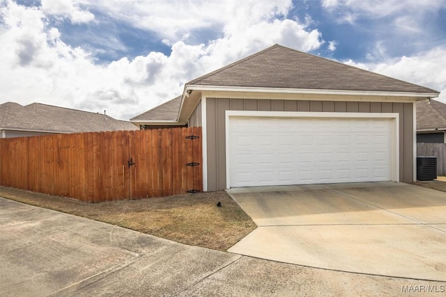 garage featuring central AC unit, concrete driveway, and fence