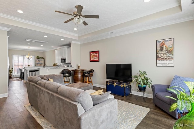 living room with a tray ceiling, ornamental molding, dark wood-type flooring, and a textured ceiling