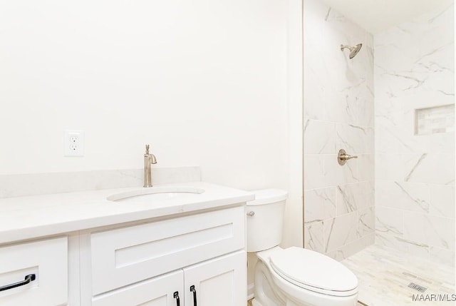 full bathroom featuring a tile shower, toilet, and vanity