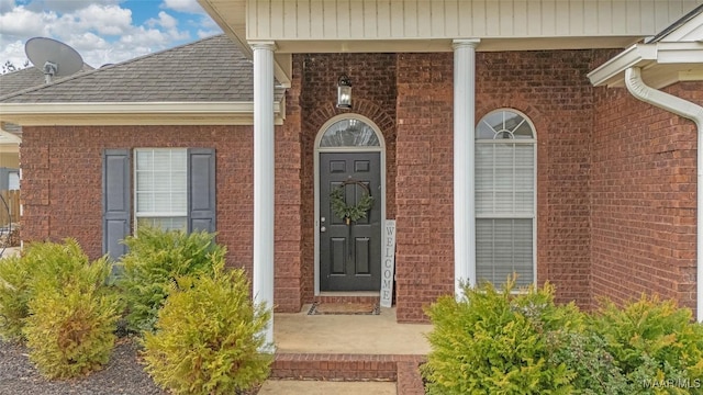 entrance to property featuring brick siding, roof with shingles, and covered porch