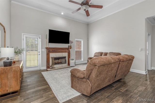 living area featuring baseboards, ceiling fan, ornamental molding, a tile fireplace, and dark wood-style floors