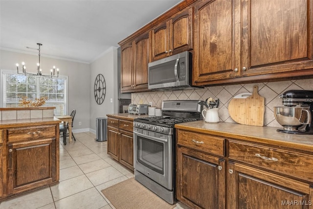 kitchen with tasteful backsplash, appliances with stainless steel finishes, an inviting chandelier, crown molding, and light tile patterned floors