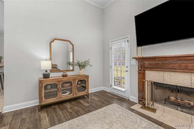 living area featuring a tiled fireplace, wood finished floors, baseboards, and ornamental molding