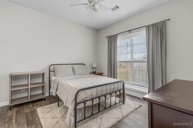 bedroom with ceiling fan, wood finished floors, visible vents, and baseboards