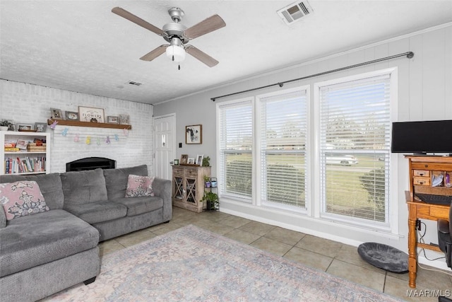 living area with visible vents, brick wall, a fireplace, ceiling fan, and tile patterned flooring