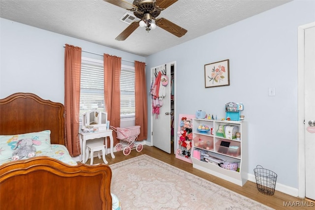 bedroom featuring visible vents, a textured ceiling, wood finished floors, baseboards, and ceiling fan