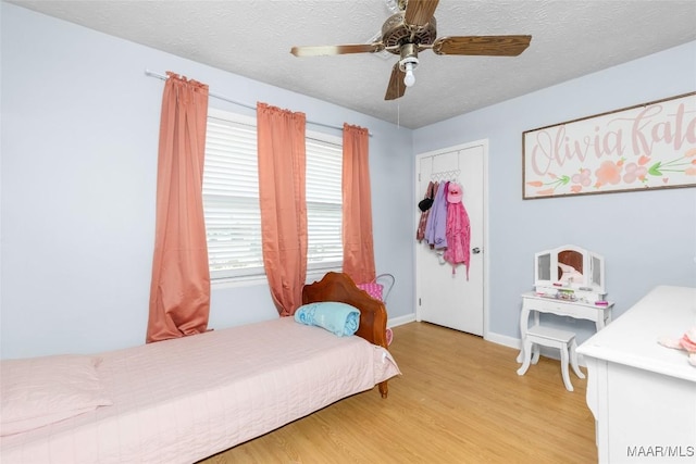 bedroom with a textured ceiling, light wood-type flooring, baseboards, and a ceiling fan