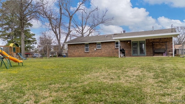 back of house featuring a lawn, brick siding, and a playground