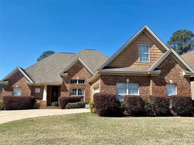 craftsman-style home featuring a garage, brick siding, a front yard, and a shingled roof