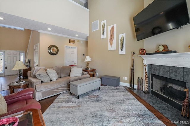 living area featuring visible vents, ornamental molding, a towering ceiling, and wood finished floors