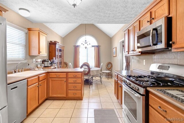 kitchen with lofted ceiling, light tile patterned floors, a peninsula, stainless steel appliances, and a sink