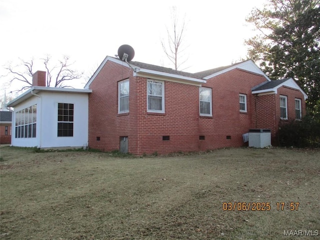 back of property featuring crawl space, a lawn, brick siding, and a chimney