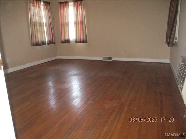 empty room featuring visible vents, wood finished floors, and baseboards
