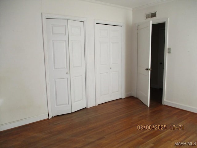 unfurnished bedroom with visible vents, two closets, ornamental molding, and dark wood-style flooring