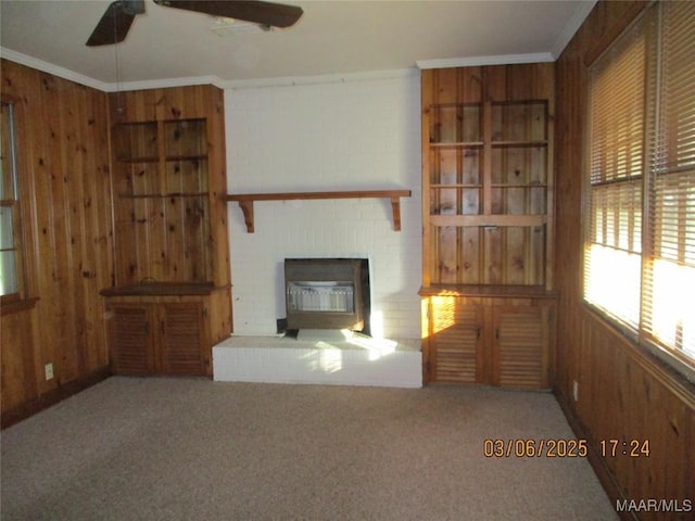 unfurnished living room with wood walls, a fireplace, crown molding, and a ceiling fan