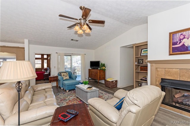 100 Royal Dr, Equality, AL 36026 - living room featuring a tiled fireplace, a textured ceiling, wood finished floors, lofted ceiling, and ceiling fan