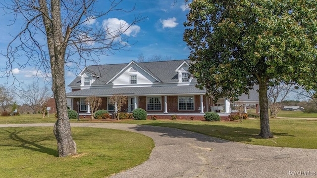 view of front of house featuring a front lawn, curved driveway, covered porch, a shingled roof, and brick siding