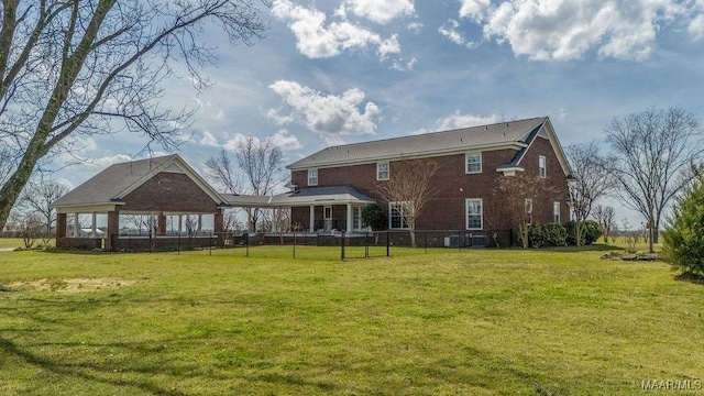 rear view of house featuring a yard, brick siding, and fence