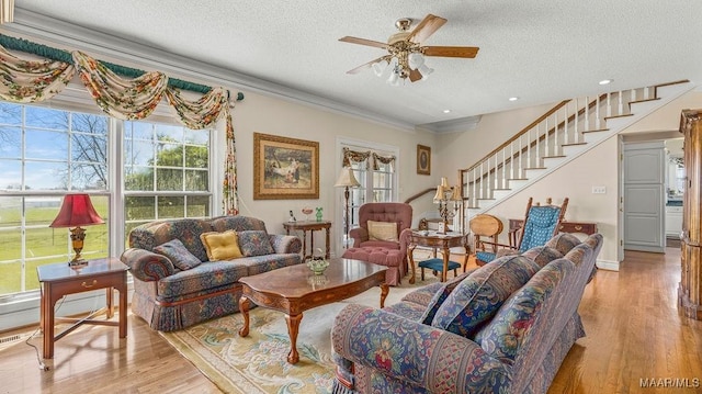 living room featuring stairway, a ceiling fan, light wood-style flooring, ornamental molding, and a textured ceiling