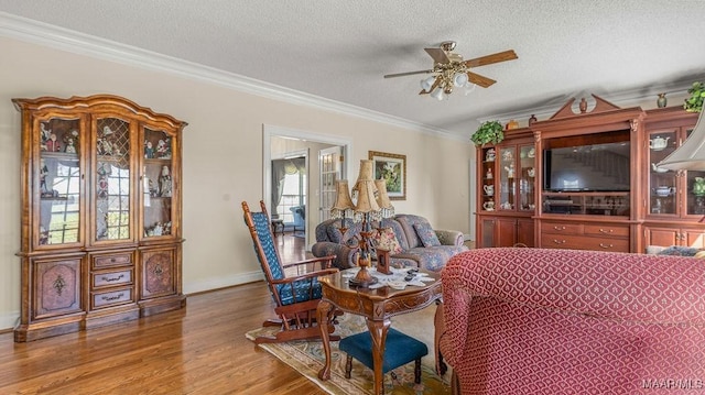dining space featuring ornamental molding, a ceiling fan, a textured ceiling, wood finished floors, and baseboards