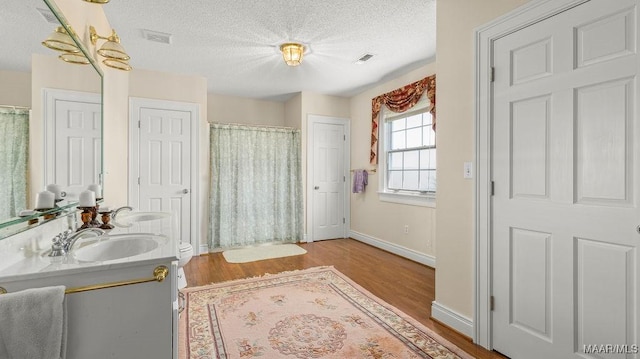 full bath with a textured ceiling, wood finished floors, visible vents, and a sink