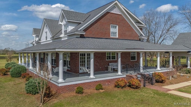 rear view of property featuring a porch, a lawn, brick siding, and roof with shingles