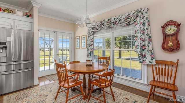 dining area with light wood-style floors, a textured ceiling, ornamental molding, and a notable chandelier