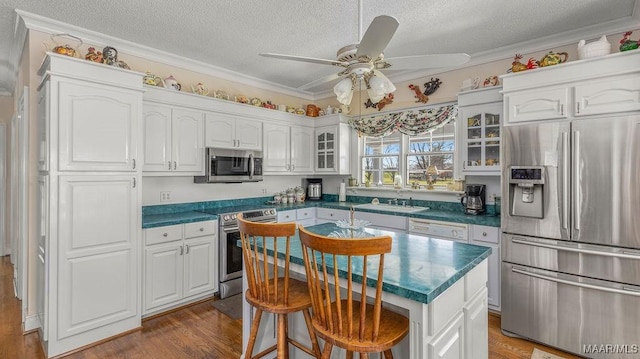 kitchen with dark countertops, ceiling fan, ornamental molding, appliances with stainless steel finishes, and white cabinetry