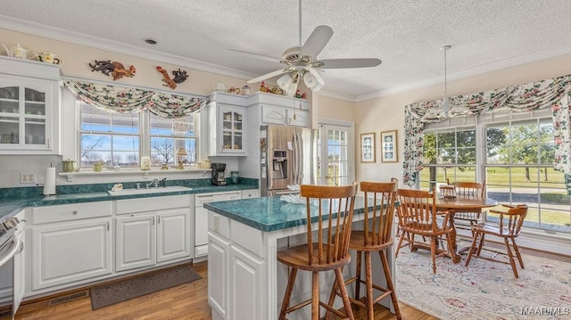 kitchen with dark countertops, glass insert cabinets, ceiling fan, appliances with stainless steel finishes, and light wood-style floors