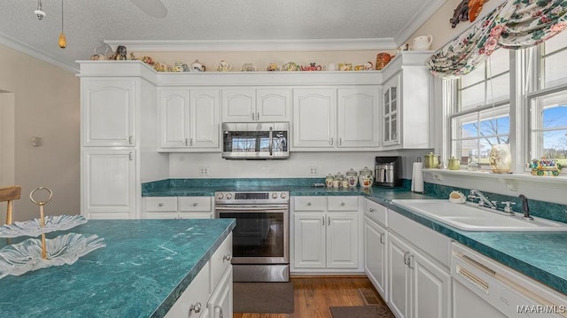 kitchen with ornamental molding, appliances with stainless steel finishes, white cabinets, a textured ceiling, and a sink