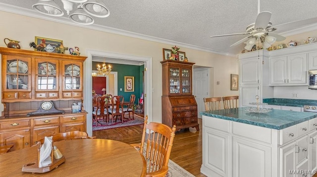 kitchen with ornamental molding, ceiling fan with notable chandelier, stainless steel microwave, wood finished floors, and white cabinets