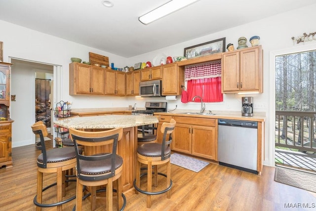kitchen with a breakfast bar, a sink, light wood-style floors, appliances with stainless steel finishes, and a center island