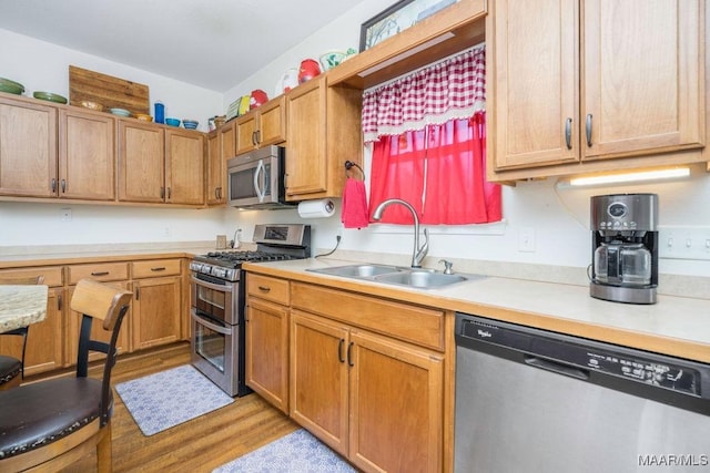 kitchen with a sink, light wood-style floors, appliances with stainless steel finishes, and light countertops