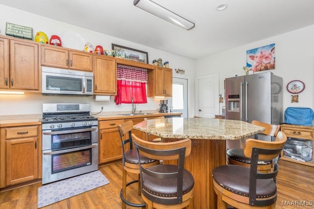 kitchen with wood finished floors, a kitchen island, appliances with stainless steel finishes, and a sink