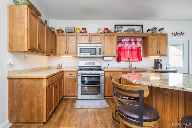 kitchen featuring brown cabinets, a breakfast bar, a sink, dark wood-style floors, and stainless steel appliances