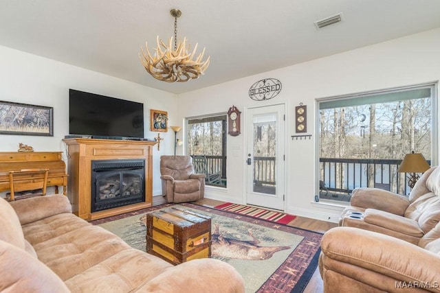 living area featuring visible vents, a glass covered fireplace, wood finished floors, baseboards, and a chandelier