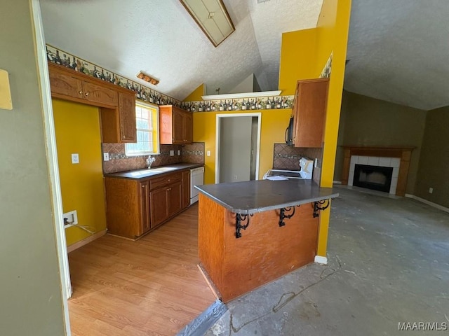 kitchen with stove, lofted ceiling, dishwasher, a peninsula, and brown cabinetry