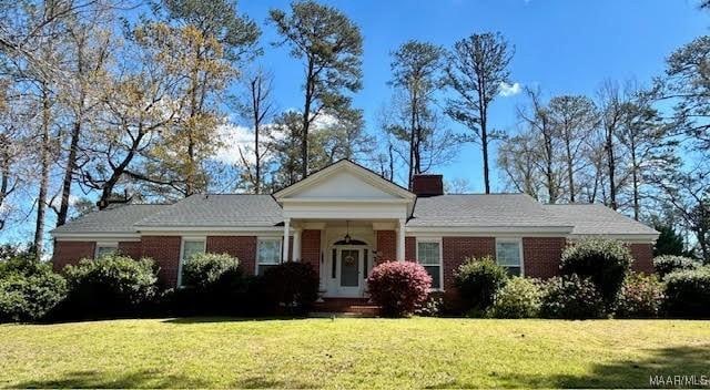 greek revival inspired property with a chimney, brick siding, and a front lawn
