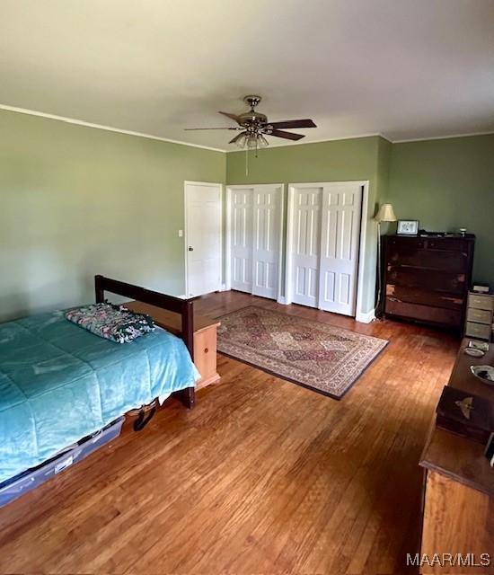 bedroom with two closets, wood finished floors, and a ceiling fan