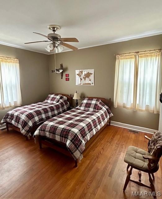 bedroom with baseboards, wood finished floors, ceiling fan, and ornamental molding