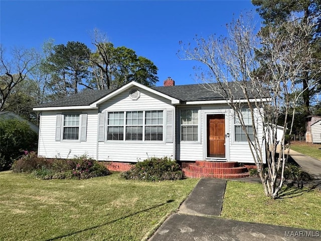 view of front facade with a front yard, a shingled roof, and a chimney