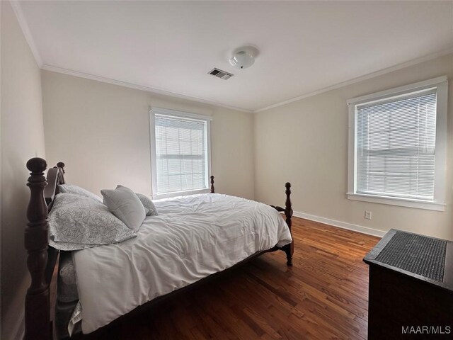 bedroom with baseboards, visible vents, crown molding, and wood finished floors