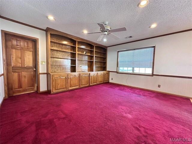spare room with crown molding, a textured ceiling, wainscoting, visible vents, and ceiling fan